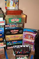 Stack of board games with focus on various Monopoly editions, Guinness World Records game, and Texas Hold 'Em poker set in front