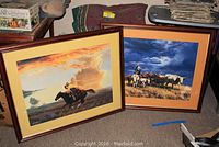 Two framed prints by A.T. Cox leaning against a wall showing Western scenes with horse riders and cattle.