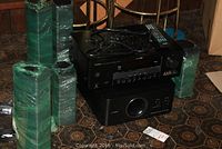 Yamaha receiver, subwoofer, remote, and wrapped speakers on a tiled floor with chairs in background.