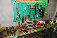 Workbench and pegboard showing assorted hand tools including chisels, planes, wrenches, pliers and clamps