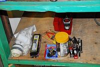Items displayed on a green wooden shelf: small parts container, mouse trap, electrical wires, pliers, and mouse trap