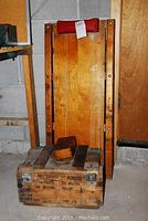 Wooden wheeled truck seen standing vertically showing the base and wheels, with the small wood box on top and the ammo box beneath it.