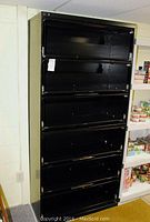 Frontal view of the black metal filing cabinet showing all 5 shelves open and the wear on the finish.