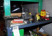 Wide angled photo of top shelf showing drill bits, containers, vintage oil can, and small tools.