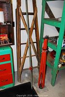 Wooden step ladder leaning against wall next to green shelving and red cabinet, showing entire ladder structure.