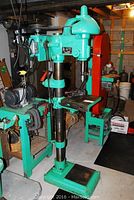 Full view of green Canadian floor drill press showing base, column, drill head and pulley assembly