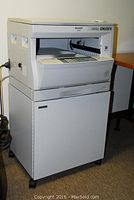 Front view of Sharp AR 163 copier on stand, plugged in, showing control panel and paper output area
