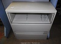 Front view of vertical filing cabinet showing three drawers, top drawer open to show metal file guides and rails.