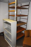Photo showing a white metal bookshelf with adjustable shelves next to a taller metal frame shelving with wooden shelves.