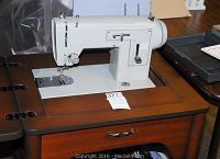 Sears Kenmore sewing machine mounted in wooden cabinet with drawer and fold-out surface.