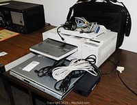 View of Acer laptop with power cords and various cables laying on top along with laptop case in background.