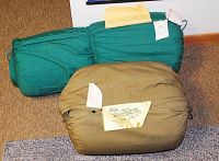 Two rolled sleeping bags, one green Forest King and one olive Mountaineer, shown on carpeted floor.