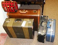 Photo shows five vintage items: three larger suitcases and two smaller items including a lunch box in checked pattern.