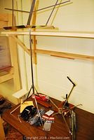 Standing metal music stand with adjustable height and a few cables arranged at base alongside microphone stand and other accessories on wooden surface.