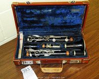 Clarinet fully disassembled inside a hard case with blue interior lining, showing all wooden body sections and keys.