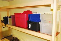 Shelf with assorted storage totes including large red, black with blue lid, and translucent with white lid; aluminum case; and black carry bag.