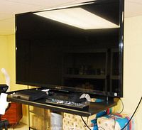Front view of Sony TV on rolling stand with shelf holding remote and cable