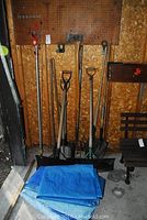 Image showing multiple long-handled garden tools including shovels and a blue tarp folded on the ground.