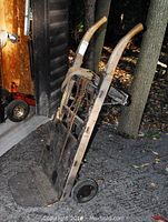 Full view of the hand truck cart showing wooden handles, metal frame, and rubber wheels positioned upright outside.