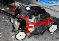 Side view of red Toro mower on gravel showing deck, wheels, handle