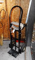 Full view of the black metal dolly standing upright with white rope coiled and attached to the handle inside wooden shed.