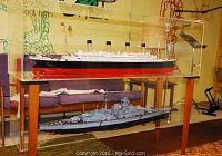 Both model ships in clear acrylic display case on wooden stand