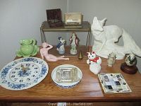 Overview of assorted decorative pieces on surface including clock, ceramic figurines, fox statuette, maneki-neko cat, plates, and small decorative items