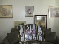 Photo showing six framed art prints displayed on a green couch and mounted on a wall including floral triptych and other nature-themed works
