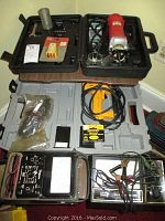 Full view of all four items displayed on table, including rotary zip tool and electric stapler in cases, engine analyzer and volt-ohm-ammeter with leads and clamps.
