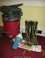 Red wet/dry 6 gallon shop vac with hose, a Black & Decker handheld vacuum, and pair of green/tan men's boots shown on red carpet.
