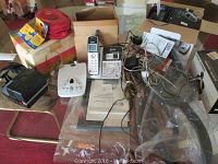 Various cameras, film packs, and a cordless home phone with base unit, cables, and chargers arranged on tabletop