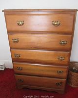 Front view of the wooden 5 drawer dresser showing brass handles and natural wood tone.