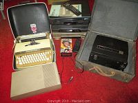 Photo of Smith Corona Coronet Electric typewriter in case, Anscovision 788 reel to reel projector in metal case, three VCRs (Panasonic PV-2301, White Westinghouse WV-328, RCA VR633HF), Commodore 1541 floppy disk drive, VHS tape collection with tape cases shown.