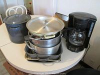 Overview of assortment of pots and pans with Mr. Coffee coffee maker on white round table