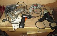 Photo showing four electric drills of different brands and styles on a wooden surface.