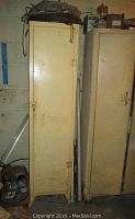 Tall narrow beige metal cabinet with single door, visible rust and wear.
