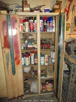 Full view of wooden shelving unit containing assorted spray cans, small boxes, and hardware items. Cans include various brands and types such as Rust-oleum and Gunk degreasers.