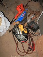 Electric hedge trimmer, circular saw, hand saws, chain, battery tender all displayed on floor in garage.