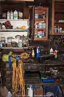 Wide view of workbench showing various cans, small hardware items on shelves, yellow extension cords, Panasonic stereo, and hand tools.