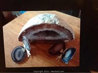 Image shows the large quartz geode cut and polished open to reveal crystalline interior beside two blue butterfly agate pieces on wooden bases shaped like butterflies.
