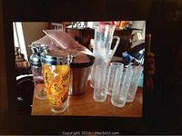 Full view of crackle glass set with pitcher and tumblers, stainless steel ice bucket, and vintage shaker on wooden table.