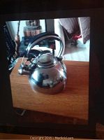 Full view of stainless steel kettle with black handle on wooden table