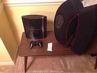 Black Sony PlayStation 3 console, controller, and gaming seat on carpeted floor and small wooden table.