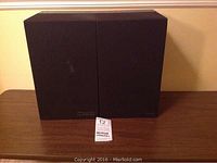 Pair of black Mission MKII Model 70 bookshelf speakers displayed side by side on a wooden surface, front view with grille cover on.