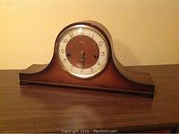 Front view of the vintage Ergo mantle clock showing the wooden case, curved top design, dual-tone clock face with Arabic numerals, and clock hands.