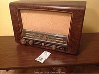 Front view showing the faux wood Bakelite casing, fabric speaker grille, tuning dial and three knobs.