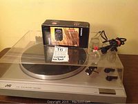 Front view of JVC L-A11 turntable with clear dust cover and box on top, showing power and speed controls, and tonearm resting on the right side.