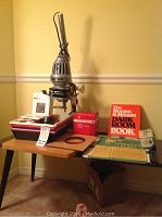 Photo showing Axomal Ia enlarger on wooden table along with developing trays, filter set in box, light bulbs, Paterson developing tank, The Morgan Dark Room Book, and small dark room accessories.