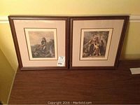 Two framed prints resting on a wooden surface, side by side, showing overall frames and matting.
