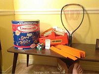 Full lot showing Tinkertoy construction set tin, orange Hot Wheels track pieces with launcher, Rubik's Cube, and small tennis racket.